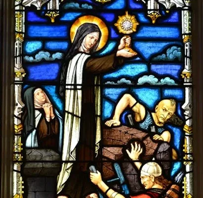 Church window showing a robed figure holding a monstrance above stonemasons at work