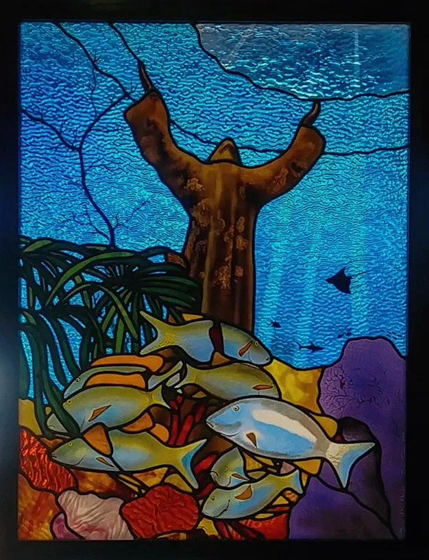 Stained glass panel of reef fish beneath a mangrove root, in blues, greens and amber